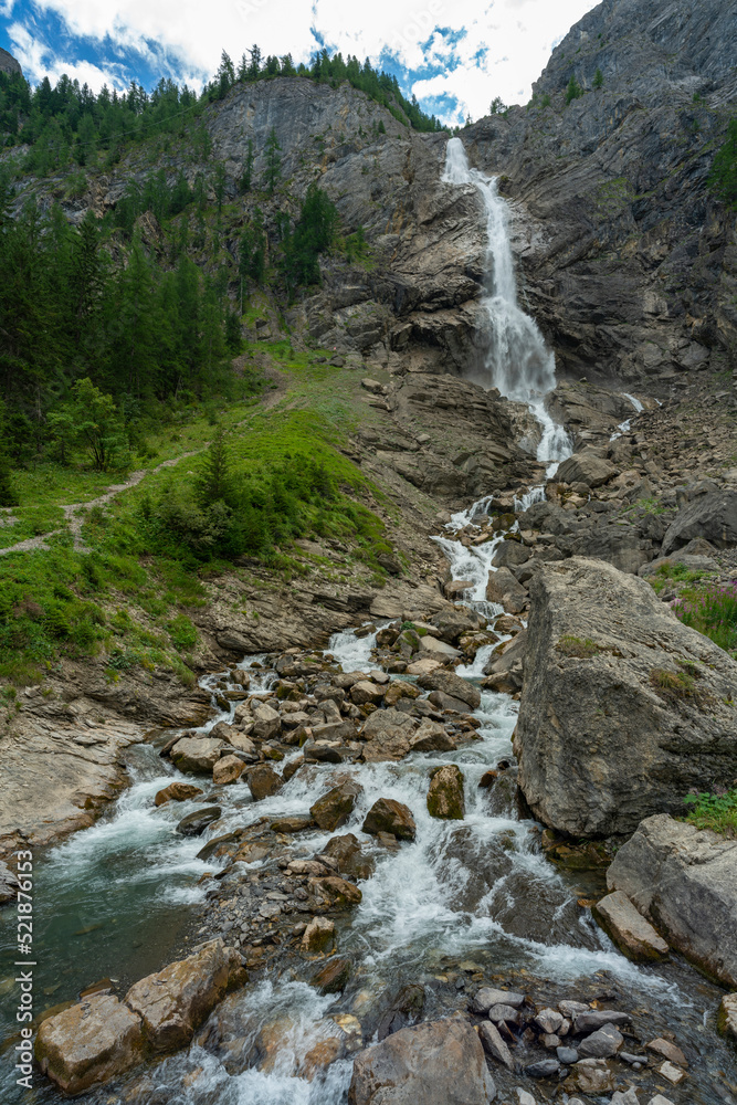 grosser Wasserfall der Engstligen in Adelboden. Das Wasser fett über eine hohe Felswand auf Geröll, Steine und Felsen. Am Ufer hat es Gras, Blumen und Bäume grosser Wasserfall der Engstligen in Adelboden. Das Wasser fett über eine hohe Felswand auf Geröll, Steine und Felsen. Am Ufer hat es Gras, Blumen und Bäume