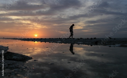 Silhouette of a man walking along the beach with his hand down and sunset in the background photo