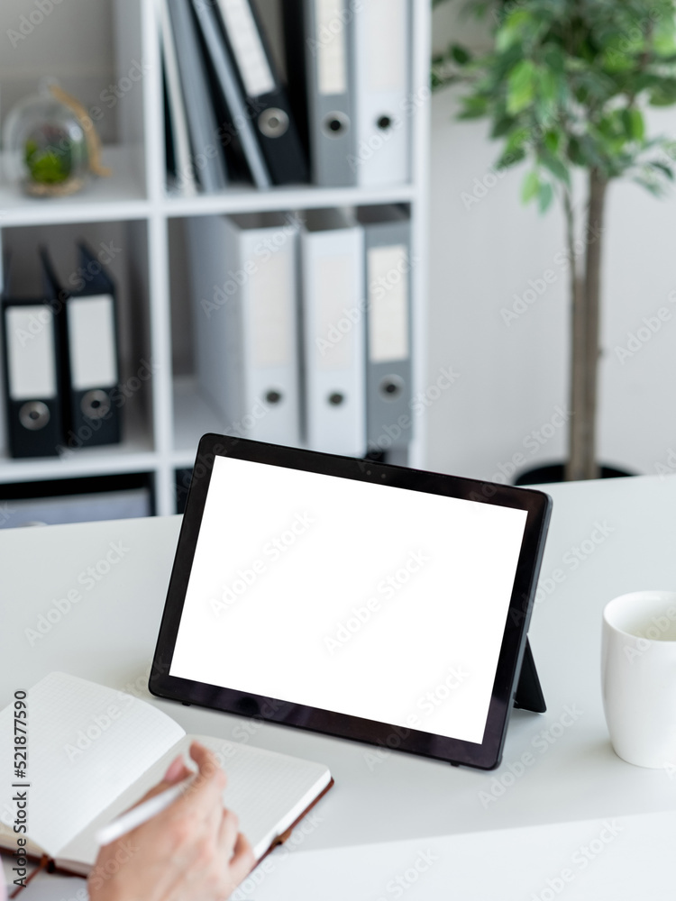 Business training. Studying woman. Computer mockup. Unrecognizable lady looking tablet computer blank screen making notes in copybook in light room interior. Business training. Studying woman. Computer mockup. Unrecognizable lady looking tablet computer blank screen making notes in copybook in light room interior.