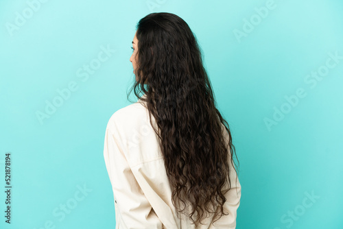 Young caucasian woman isolated on blue background in back position and looking back