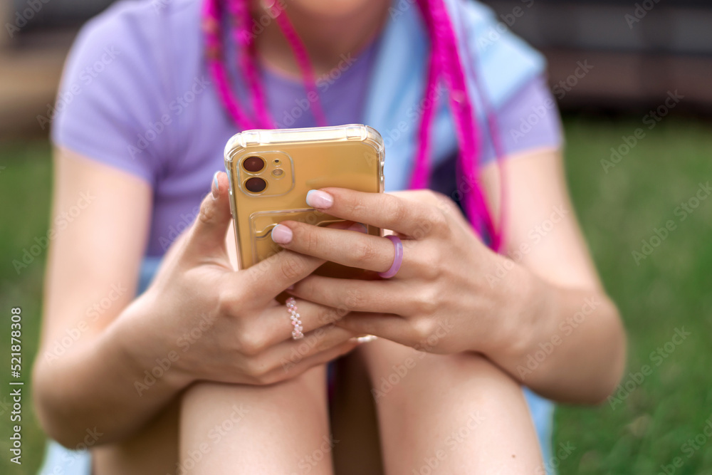 Teenage hipster girl with pink braids using a smartphone on a street background.Summer concept.Generation Z style.Social media concept.Selective focus,copy space.