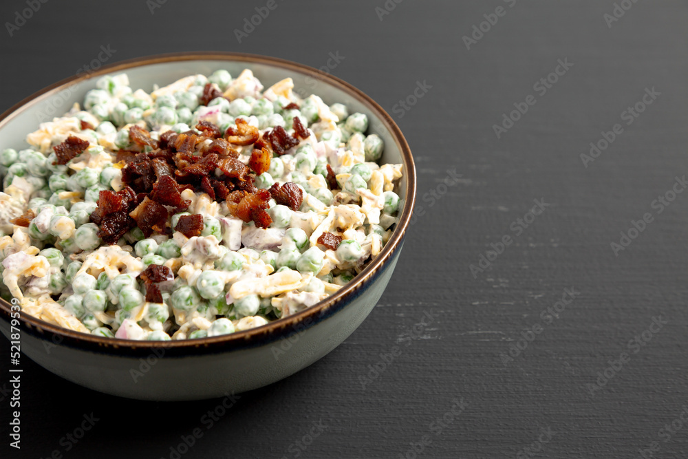 Homemade Creamy Bacon Pea Salad in a Bowl on a black background, side view. Space for text.