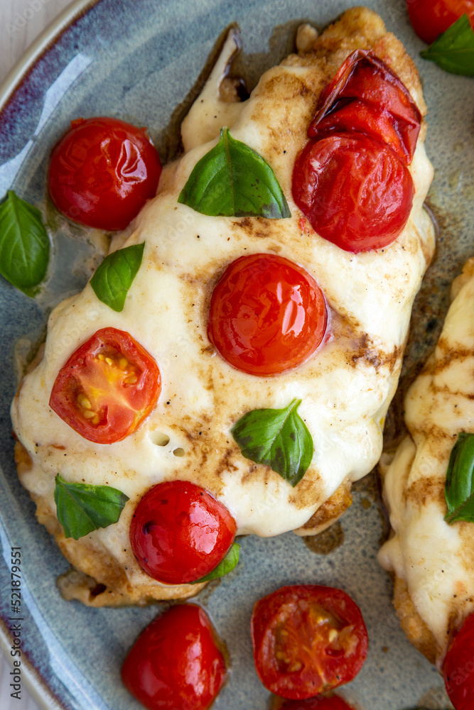 Homemade Caprese Chicken Parmesan with tomato, mozzarella and basil on a Plate, top view. Flat lay, overhead, from above. Close-up. Homemade Caprese Chicken Parmesan with tomato, mozzarella and basil on a Plate, top view. Flat lay, overhead, from above. Close-up.