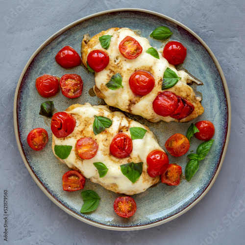 Homemade Caprese Chicken Parmesan with tomato, mozzarella and basil on a Plate, overhead view.