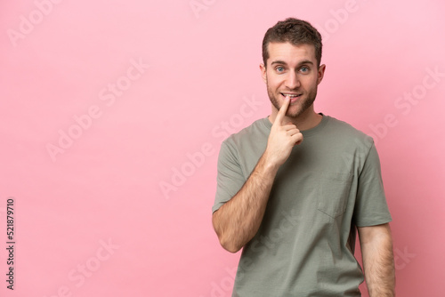 Young caucasian man isolated on pink background showing a sign of silence gesture putting finger in mouth