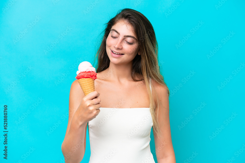 Young woman in swimsuit holding an ice cream isolated on blue background with happy expression Young woman in swimsuit holding an ice cream isolated on blue background with happy expression