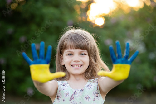 Joyful child girl waving hands painted in Ukraine flag colors and say hello outdoor at nature background  focus on hands