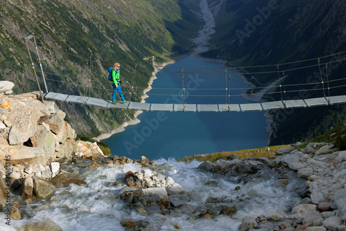 Young woman trekking over a bridge in die Zillertal Alps. Schlegeis Stausee lake view from mountain hiking path trail. Zillertal, Austria, Europe photo