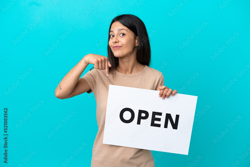 Young woman over isolated background holding a placard with text OPEN and pointing it Young woman over isolated background holding a placard with text OPEN and pointing it