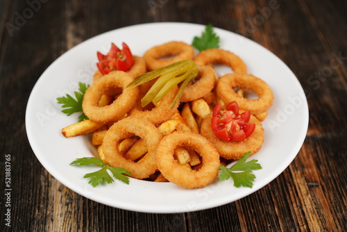 Fried french fries with onion ring in white bowl on wooden background. Fast food products; onion rings and french fries on the bowl. Unhealthy food.