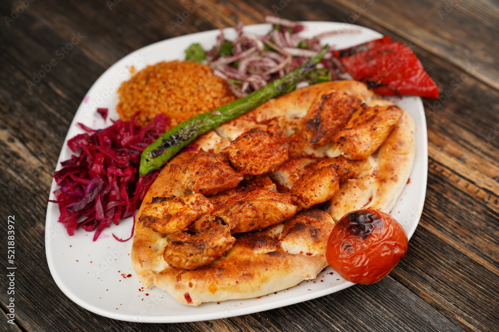 Grilled Turkish chicken wings served with pita, garnish, onions, bulgur, roasted green pepper, and roasted tomato on white plate on wooden background. Served special restaurant presentation Grilled Turkish chicken wings served with pita, garnish, onions, bulgur, roasted green pepper, and roasted tomato on white plate on wooden background. Served special restaurant presentation