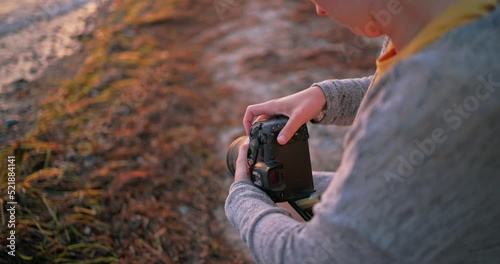 Girl taking photos with a camera at the ocean during sunset