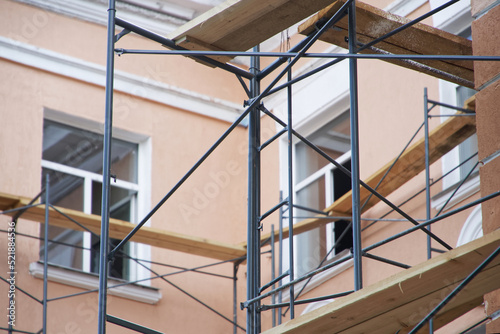 Wooden and metal scaffolding next to the outer wall, windows and roof of a multi-storey building. Repair, renovation, reconstruction and restoration of retro vintage city houses.