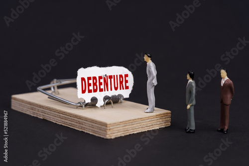Figures of businessmen stand near a mousetrap, the bait in which is torn paper with the inscription - Debenture