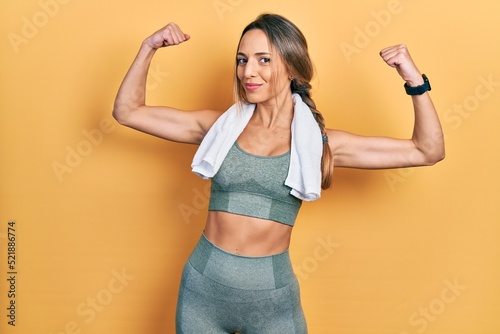 Beautiful hispanic woman wearing sportswear and towel showing arms muscles smiling proud. fitness concept.