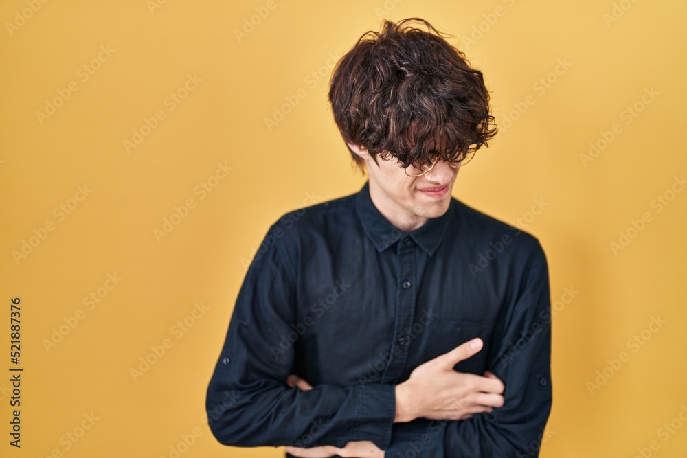 Obraz premium Young man wearing glasses over yellow background with hand on stomach because nausea, painful disease feeling unwell. ache concept.