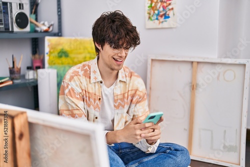 Young hispanic man artist smiling confident using smartphone at art studio