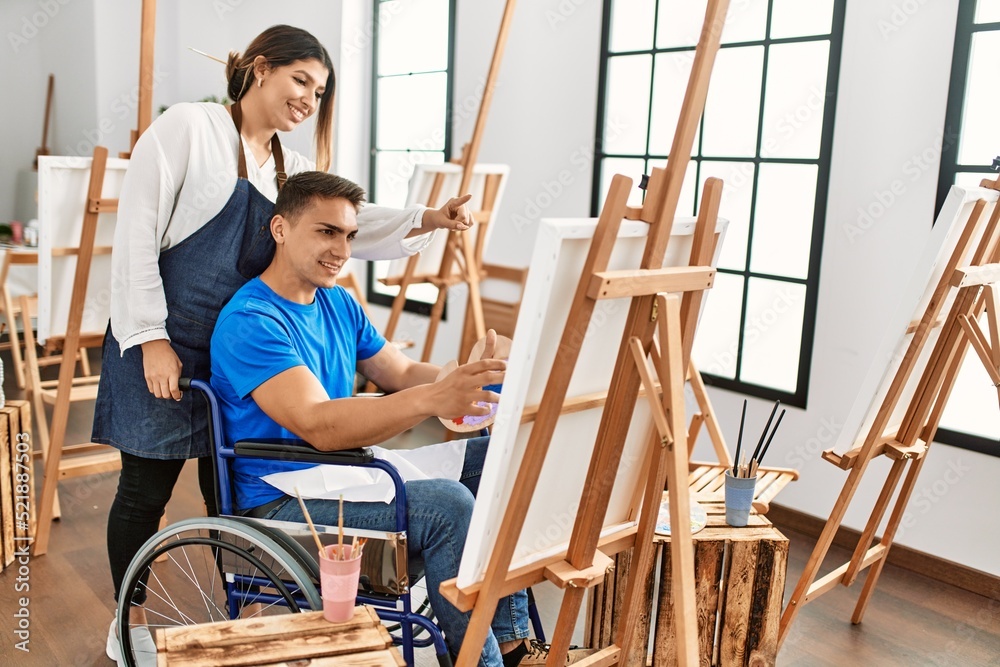 Teacher and disabled paint student sitting on wheelchair smiling happy painting at art school.