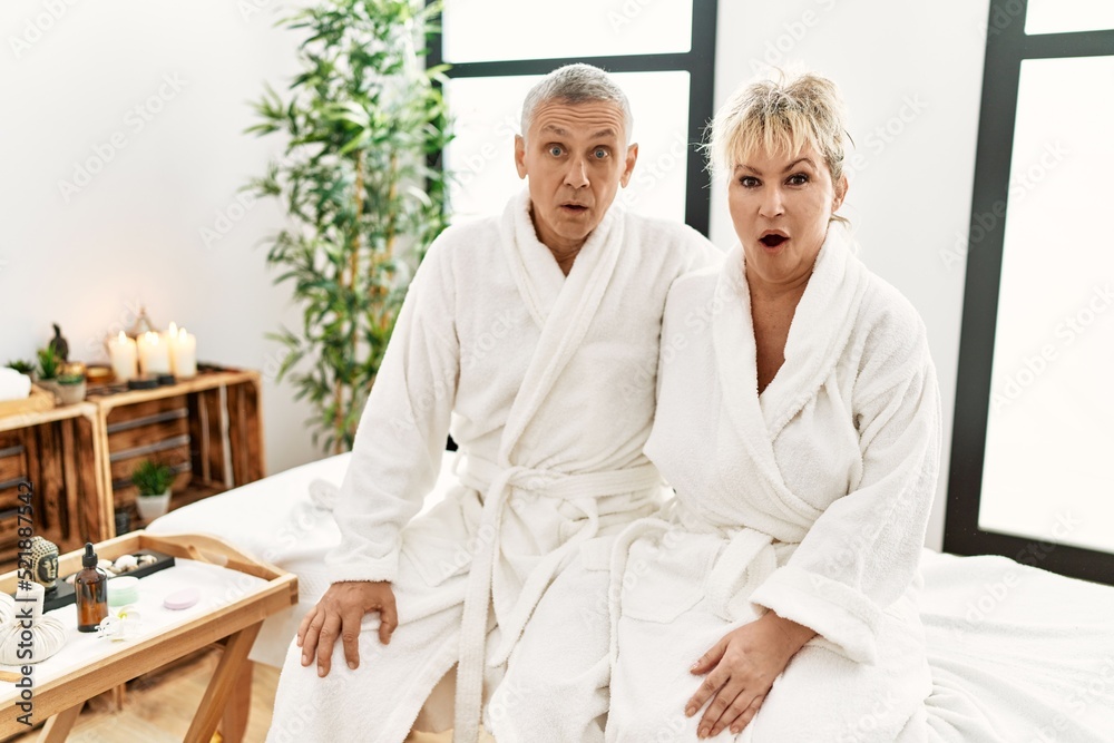 Middle age caucasian couple wearing bathrobe at wellness spa scared and amazed with open mouth for surprise, disbelief face Middle age caucasian couple wearing bathrobe at wellness spa scared and amazed with open mouth for surprise, disbelief face