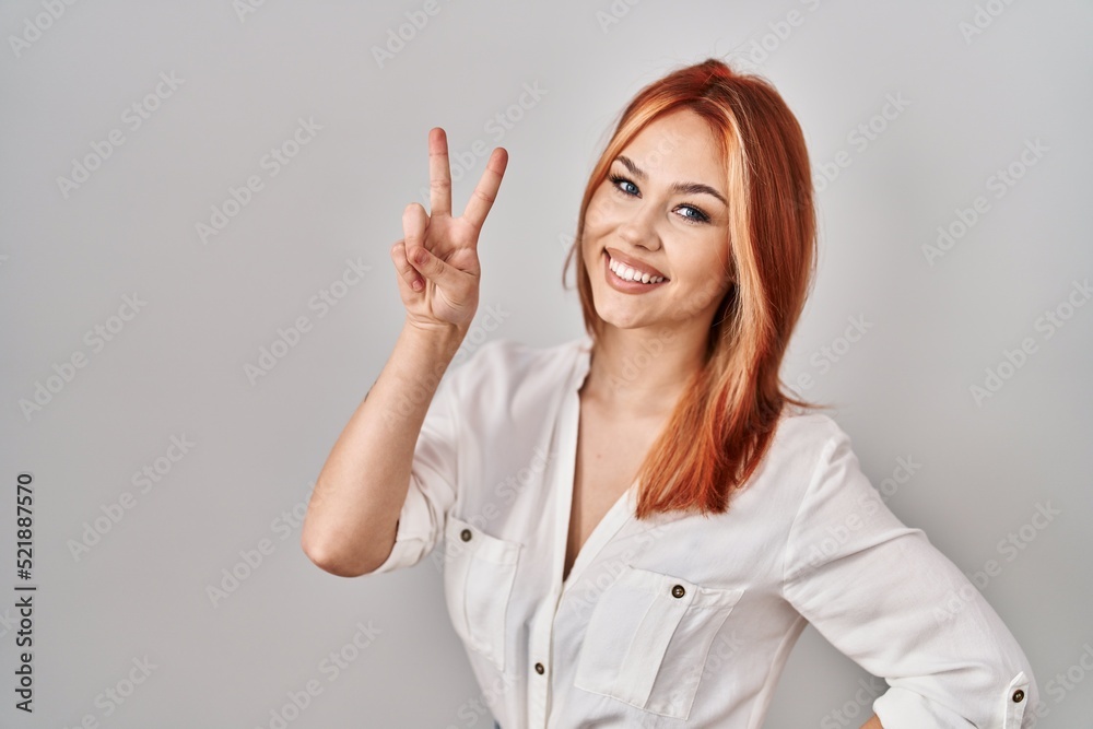 Young caucasian woman standing over isolated background smiling looking to the camera showing fingers doing victory sign. number two. Young caucasian woman standing over isolated background smiling looking to the camera showing fingers doing victory sign. number two.