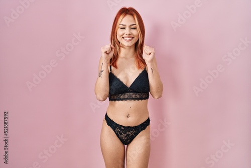 Young caucasian woman wearing lingerie over pink background excited for success with arms raised and eyes closed celebrating victory smiling. winner concept.