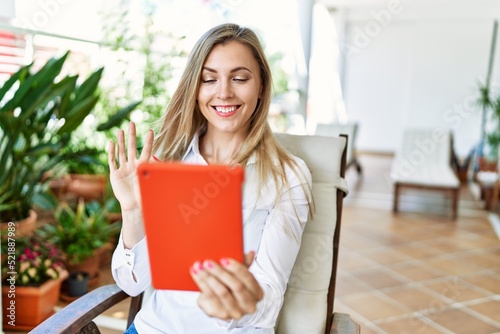 Young blonde woman smiling happy using touchpad sitting on the table at the terrace.