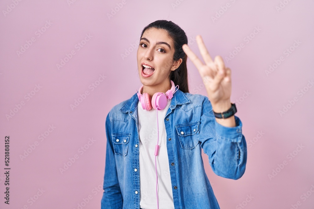 Young beautiful woman standing over pink background smiling looking to the camera showing fingers doing victory sign. number two. Young beautiful woman standing over pink background smiling looking to the camera showing fingers doing victory sign. number two.