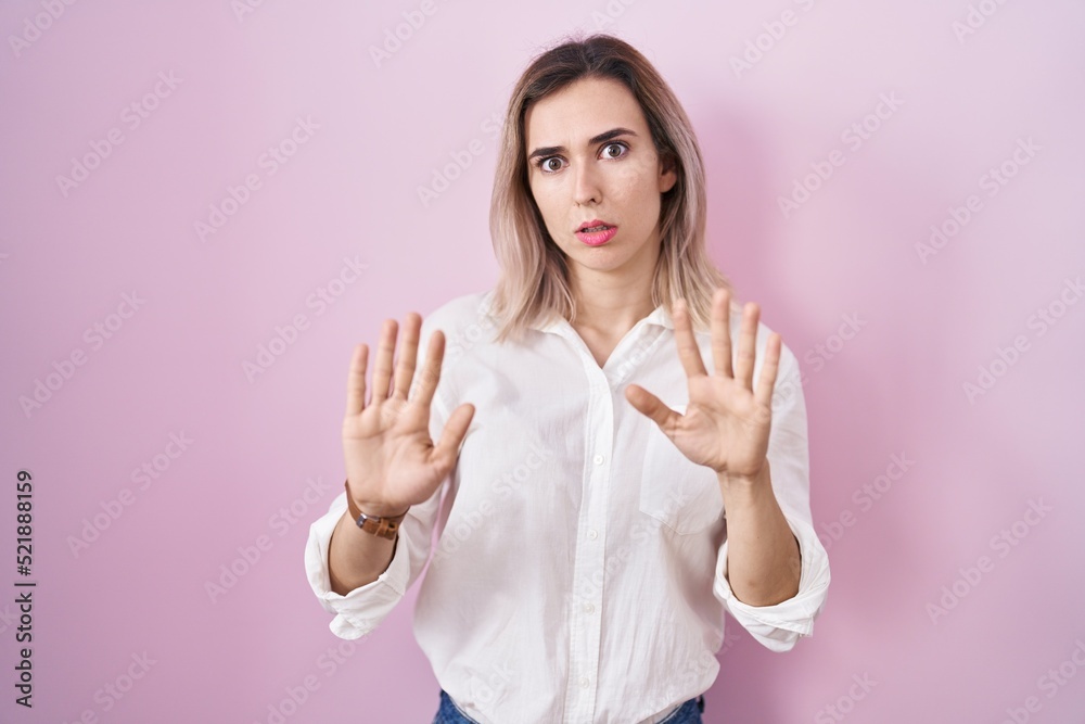 Young beautiful woman standing over pink background moving away hands palms showing refusal and denial with afraid and disgusting expression. stop and forbidden. Young beautiful woman standing over pink background moving away hands palms showing refusal and denial with afraid and disgusting expression. stop and forbidden.