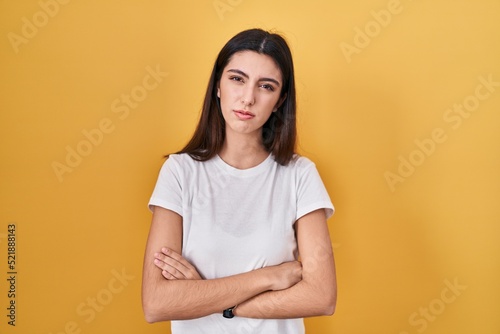 Young beautiful woman standing over yellow background skeptic and nervous, disapproving expression on face with crossed arms. negative person.