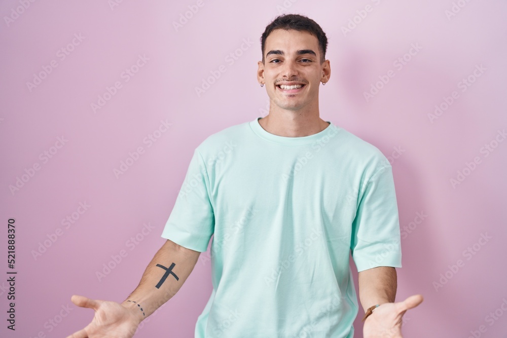 Handsome hispanic man standing over pink background smiling cheerful with open arms as friendly welcome, positive and confident greetings Handsome hispanic man standing over pink background smiling cheerful with open arms as friendly welcome, positive and confident greetings