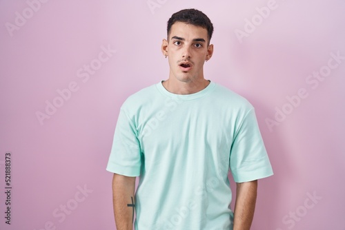 Handsome hispanic man standing over pink background in shock face, looking skeptical and sarcastic, surprised with open mouth