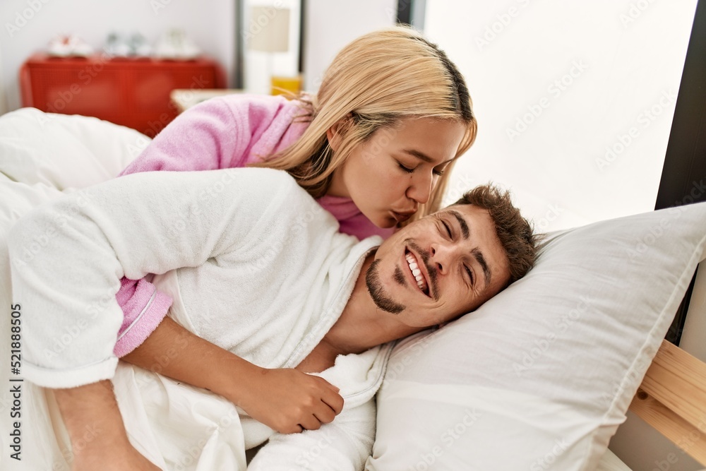 Young caucasian couple kissing and hugging lying on the bed at home.