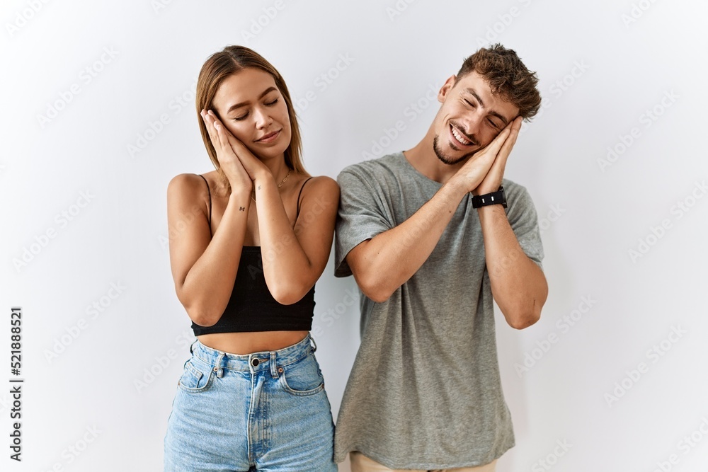 Naklejka premium Young beautiful couple standing together over isolated background sleeping tired dreaming and posing with hands together while smiling with closed eyes.