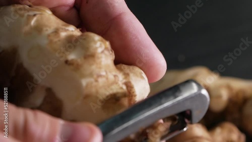 Chef peeling raw fresh jerusalem artichokes or ginger close up.