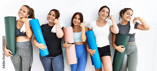 Group of women holding yoga mat standing over isolated background smiling doing phone gesture with hand and fingers like talking on the telephone. communicating concepts.