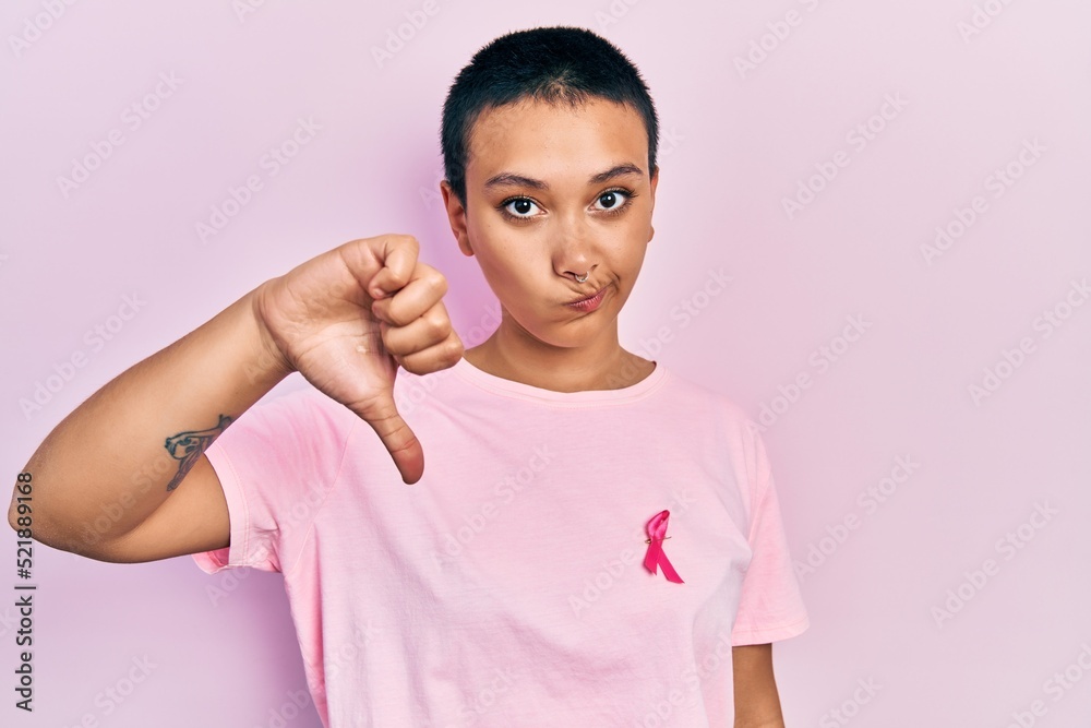 Beautiful hispanic woman with short hair wearing pink cancer ribbon on shirt with angry face, negative sign showing dislike with thumbs down, rejection concept Beautiful hispanic woman with short hair wearing pink cancer ribbon on shirt with angry face, negative sign showing dislike with thumbs down, rejection concept