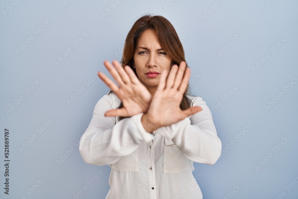 Hispanic woman standing over isolated background rejection expression crossing arms and palms doing negative sign, angry face Hispanic woman standing over isolated background rejection expression crossing arms and palms doing negative sign, angry face