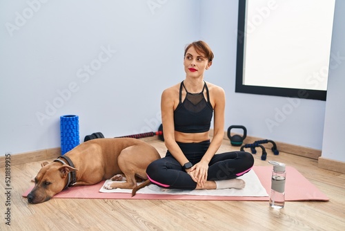 Young beautiful woman sitting on yoga mat smiling looking to the side and staring away thinking.