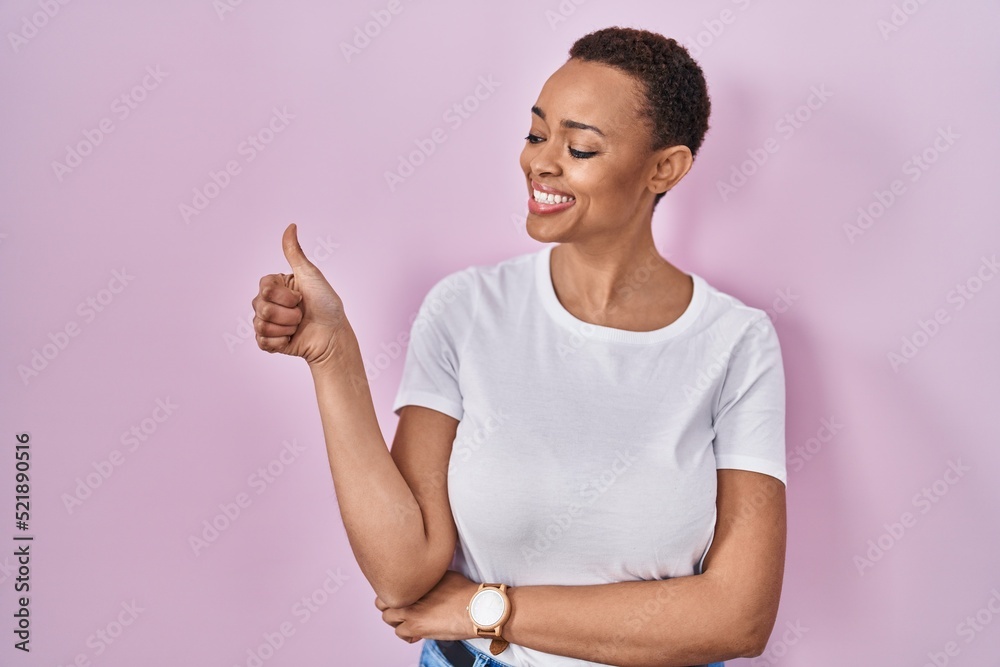 Beautiful african american woman standing over pink background looking proud, smiling doing thumbs up gesture to the side Beautiful african american woman standing over pink background looking proud, smiling doing thumbs up gesture to the side
