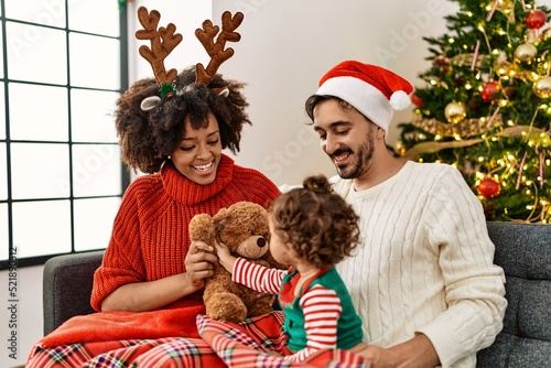 Couple and daughter playing with teddy bear sitting by christmas tree at home