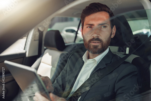 Handsome businessman working on digital tablet while sitting on driver seat in luxury car