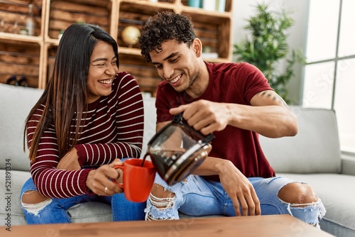 Young latin couple smiling happy drinking coffee sitting on the sofa at home.