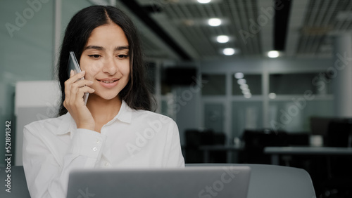 Busy female worker woman talk phone answer call arabic businesswoman do multitasking work on laptop chatting provide mobile support assistance for client in coworking office space make internet order