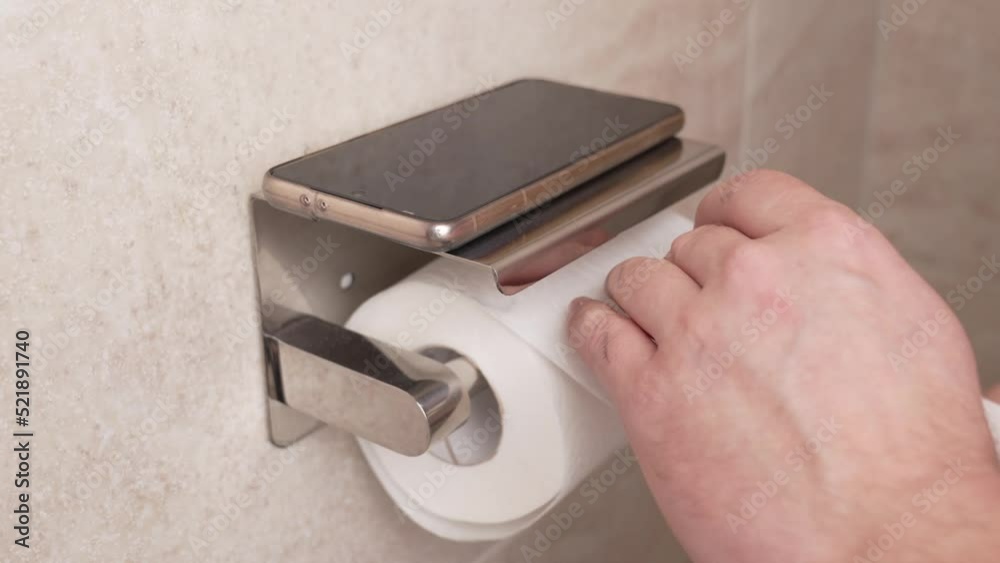 hands put the phone on the shelf unwind and tear off a piece of toilet paper. hands put the phone on the shelf unwind and tear off a piece of toilet paper.