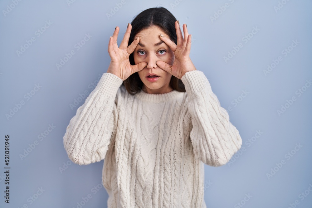 Young brunette woman standing over blue background trying to open eyes with fingers, sleepy and tired for morning fatigue Young brunette woman standing over blue background trying to open eyes with fingers, sleepy and tired for morning fatigue