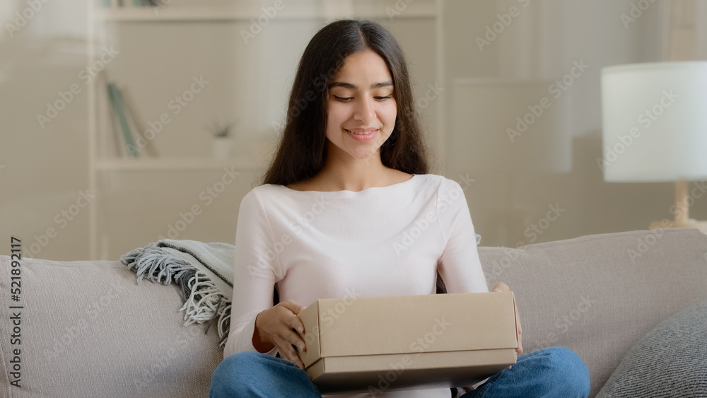 Surprised arab latin woman satisfied customer shopaholic sits on couch at home open delivery parcel postal carton box unpack present gift look at shipping goods purchases from internet clothing store Surprised arab latin woman satisfied customer shopaholic sits on couch at home open delivery parcel postal carton box unpack present gift look at shipping goods purchases from internet clothing store