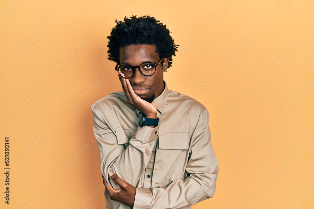 Young african american man wearing casual clothes and glasses thinking looking tired and bored with depression problems with crossed arms. Young african american man wearing casual clothes and glasses thinking looking tired and bored with depression problems with crossed arms.