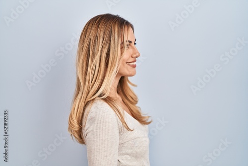 Young blonde woman standing over isolated background looking to side, relax profile pose with natural face and confident smile.