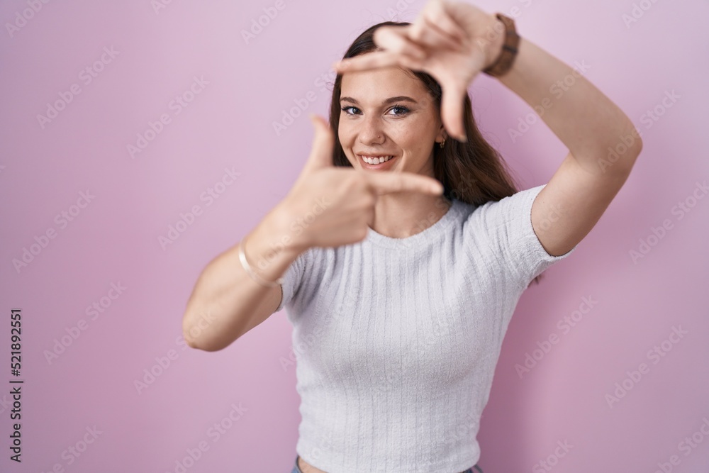 Young hispanic girl standing over pink background smiling making frame with hands and fingers with happy face. creativity and photography concept.