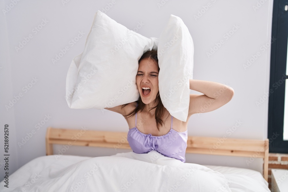 Young woman asleep for noise covering ears with pillow at bedroom Young woman asleep for noise covering ears with pillow at bedroom